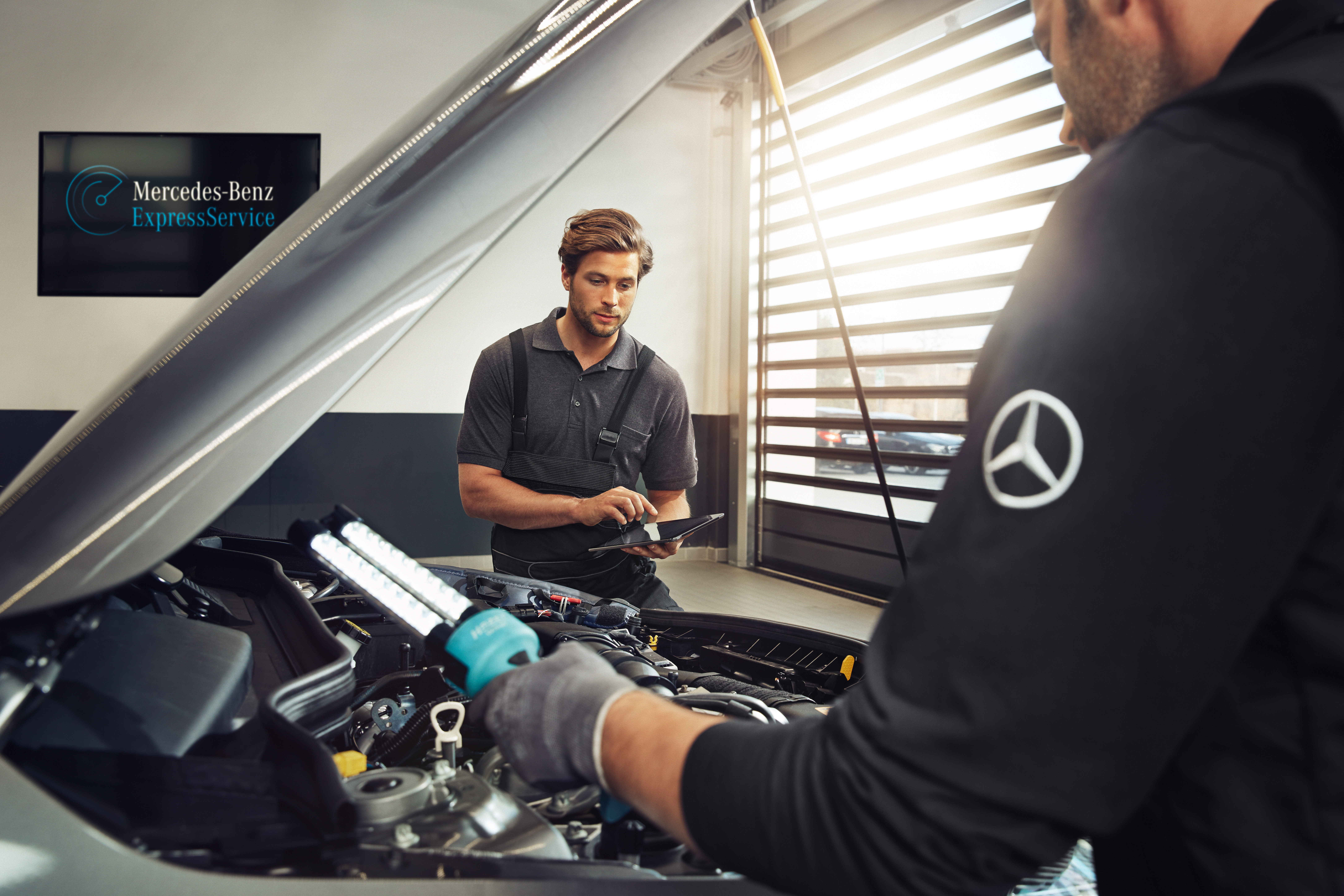 Seitliche Sicht auf eine geöffnete Motorhaube an dem zwei Monteure arbeiten