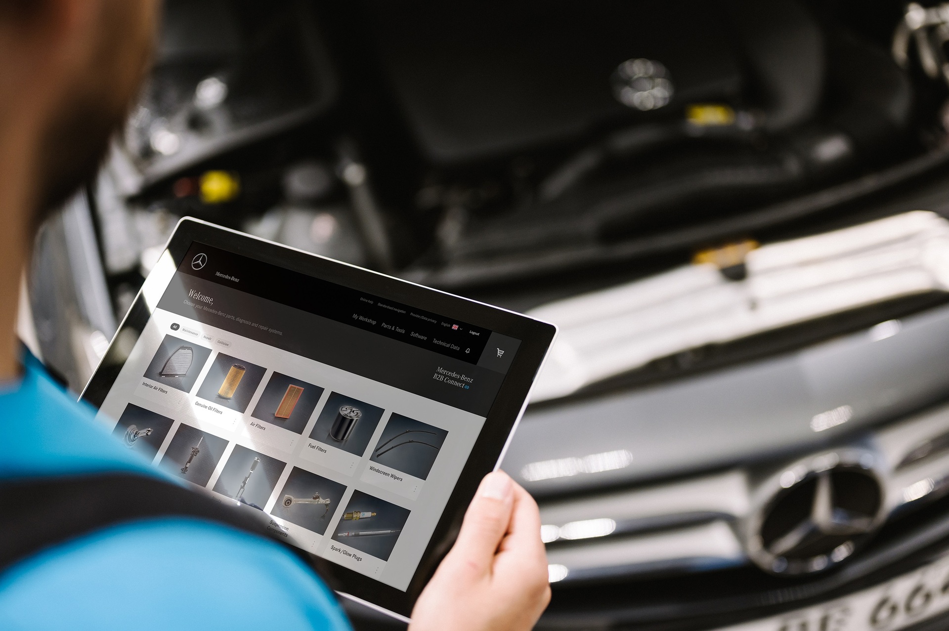 Mitarbeiter hält Tablet mit Anzeige von Fahrzeugteilen vor geöffneter Motorhaube