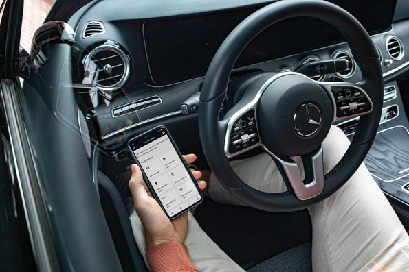 Person mit Smartphone und Mercedes-Benz App, Mercedes im Glaskasten im Hintergrund