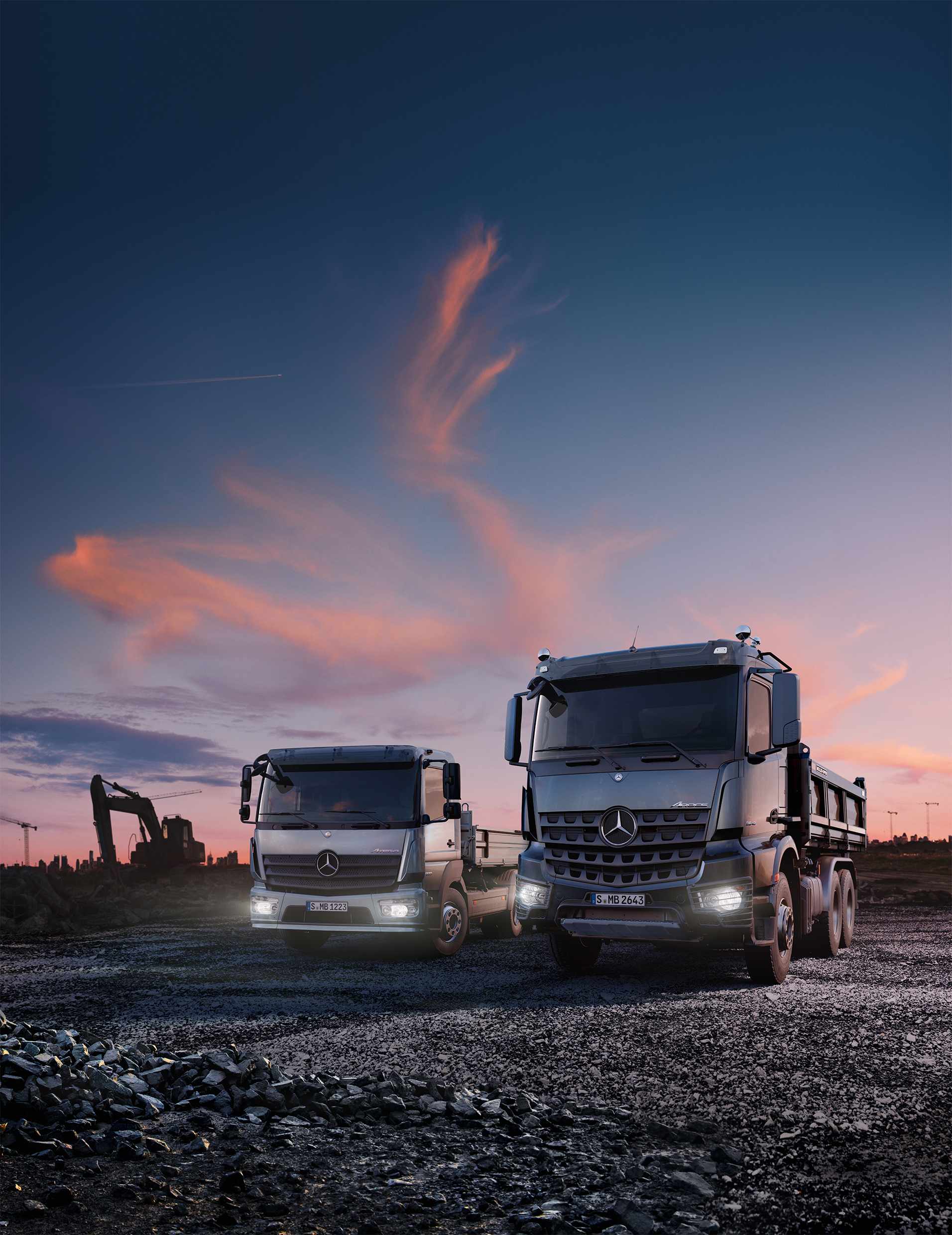 Zwei Mercedes-Benz Lkw stehen auf einer Baustelle unter dunkler werdendem Himmel