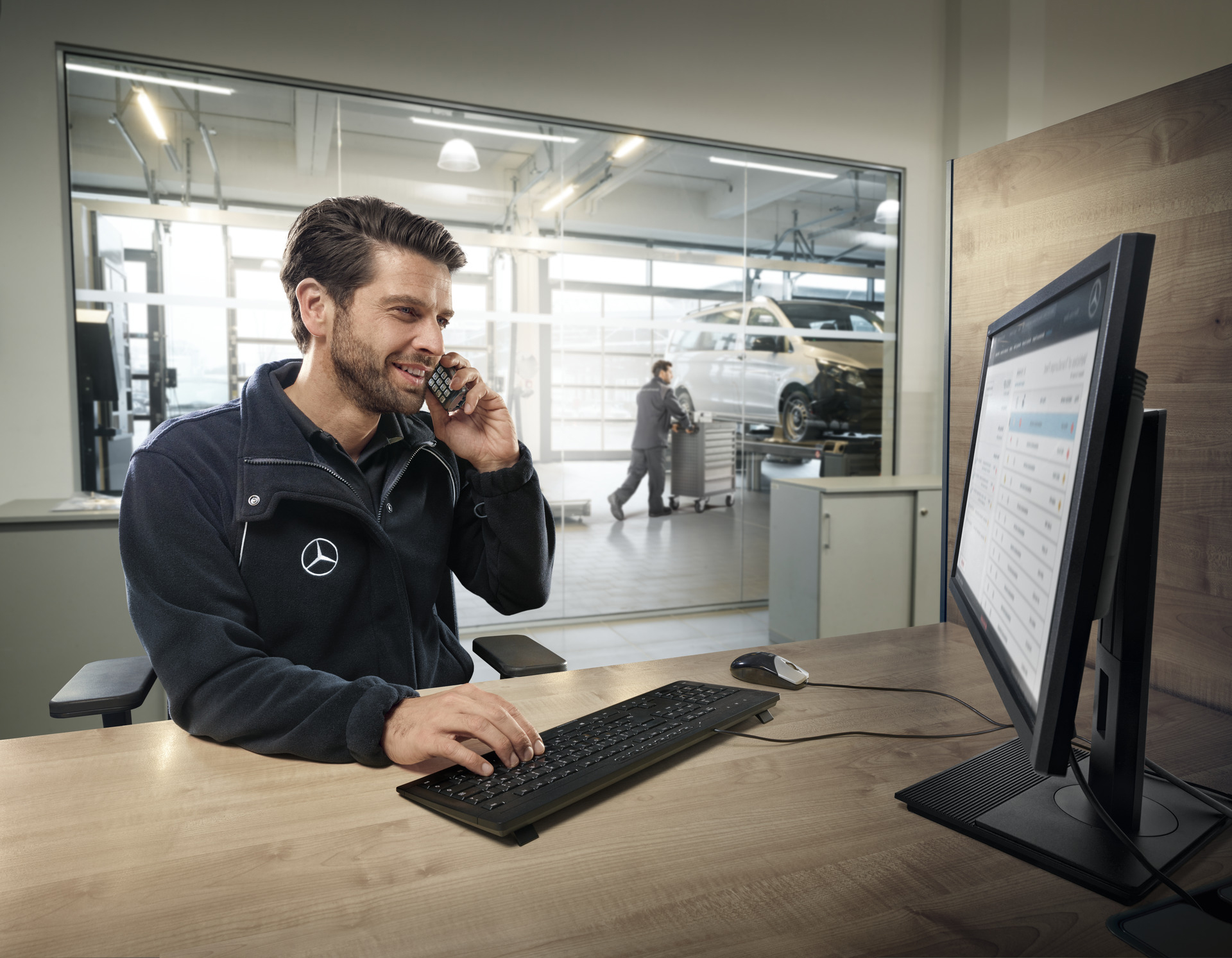 Männlicher Mercedes-Mitarbeiter sitzt in einem Büro vor seinem Computer und telefoniert