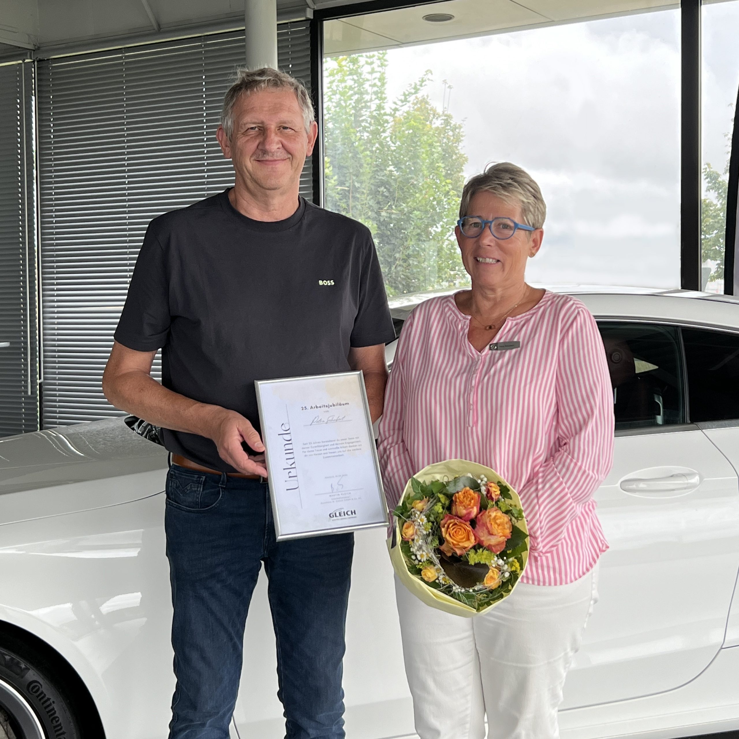 Ein Mann übergibt einer Frau eine Urkunde, die einen Blumenstrauß in der Hand hält