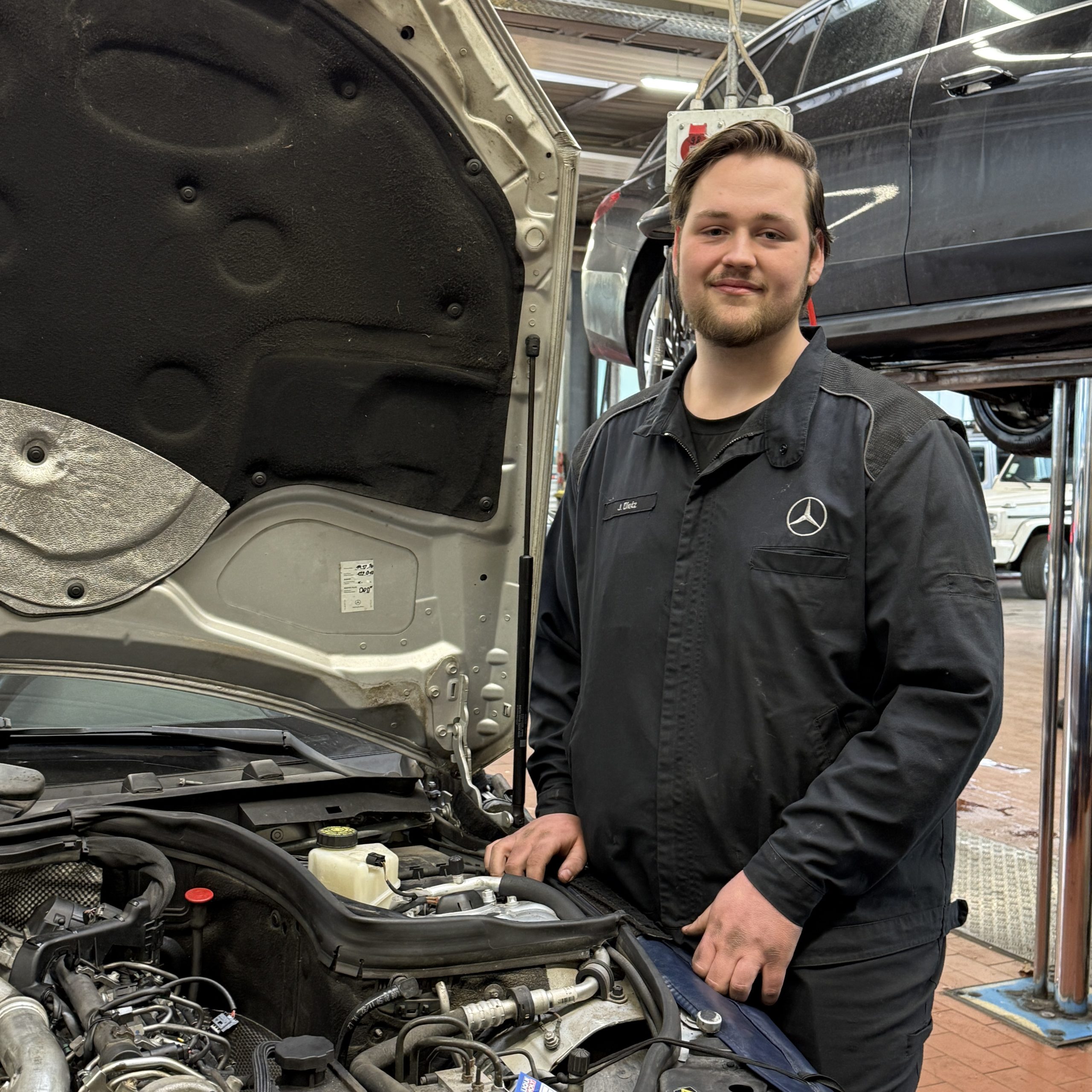 In der Werkstatt steht ein junger Mann neben einem Fahrzeug mit geöffneter Motorhaube