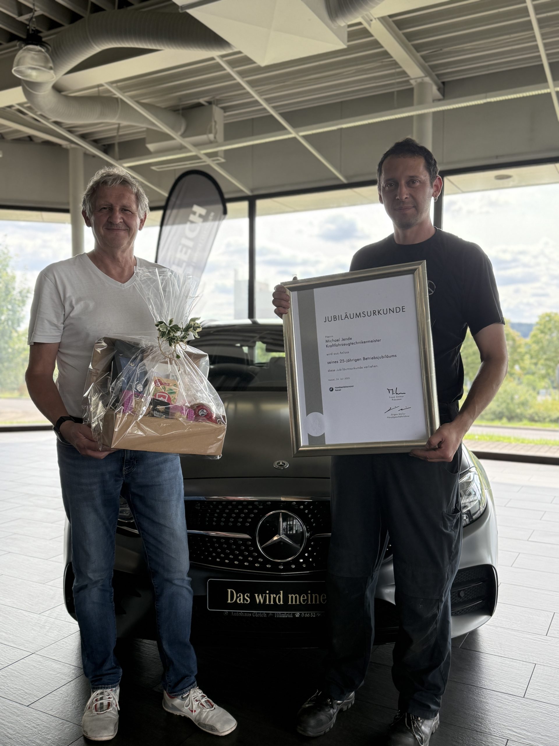 Ein Mann hält einen Präsentkorb und ein anderer Mann hält seine  Urkunde